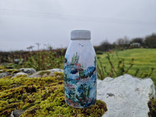 Load image into Gallery viewer, A milk bottle with sea patterns on it on a stone wall beside moss with grass and sky in the background