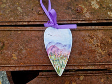 Load image into Gallery viewer, A heart with hills and grass painted on it. Placed on a rusty metal surface.