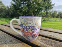 Load image into Gallery viewer, A large mug with a spongeware pattern on it, on a wooden picnic bench. Grass and a hedge in the background