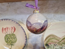 Load image into Gallery viewer, Decorative glass ball with a scenic design hanging on a purple ribbon against a white background.
