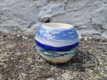 Load image into Gallery viewer, A ceramic tealight holder with a beachy design, featuring blue and white colors and a small bird, placed on a textured surface.
