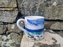 Load image into Gallery viewer, A ceramic mug with a hand-painted blue seascapes design, placed against a rocky backdrop.
