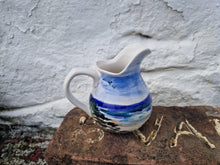 Load image into Gallery viewer, A ceramic jug with a hand-painted blue and white beach scene design, placed on a stone surface.
