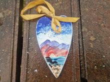 Load image into Gallery viewer, A flat heart with the hills and sea painted on it, with a ribbon and bow at the top for hanging it up.
