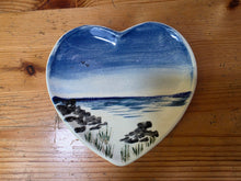 Load image into Gallery viewer, A heart-shaped ceramic plate with a hand-painted landscape design of sea and rocks, resting on a wooden table.
